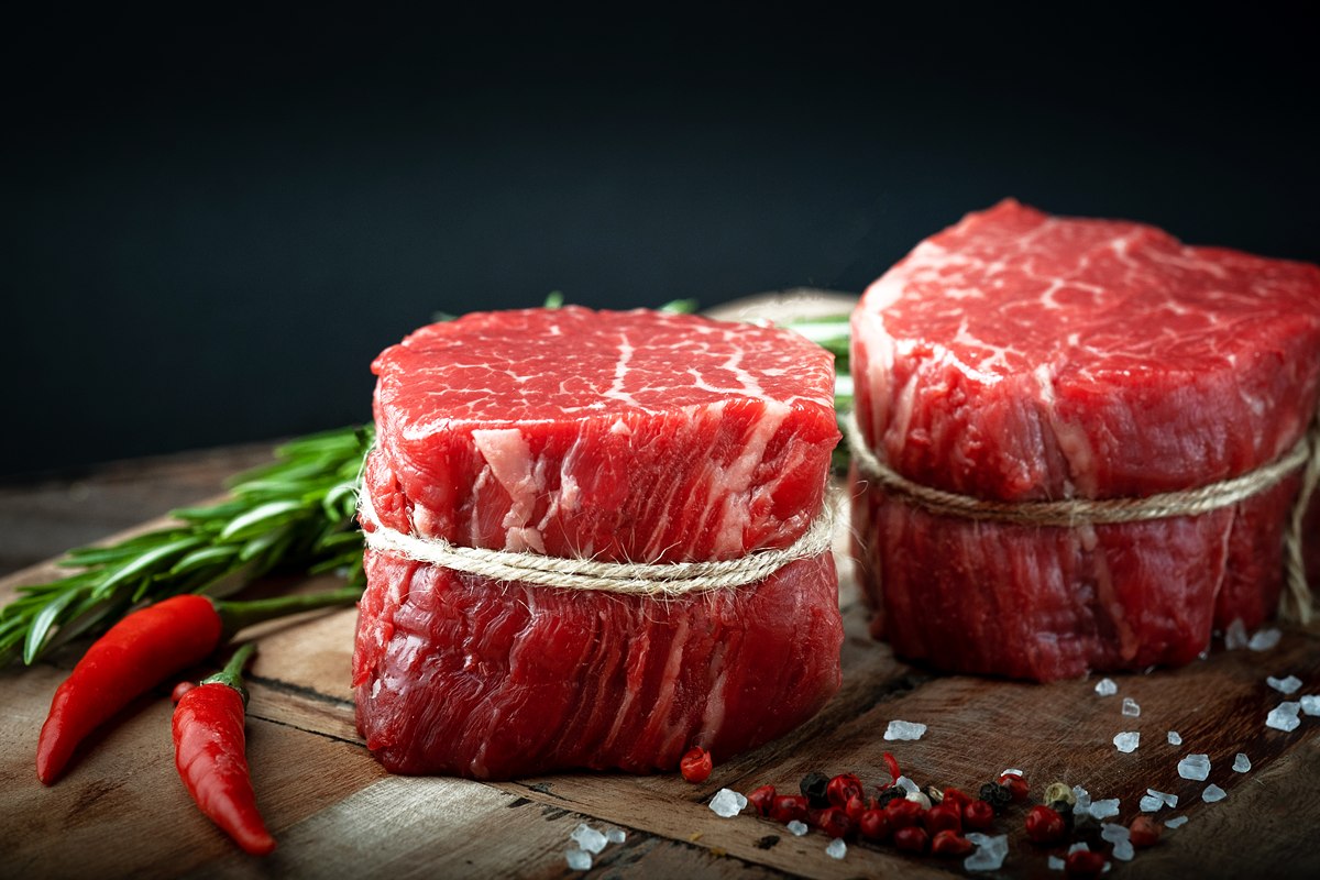 Zwei rohe, mit Küchengarn gebundene Rinderfilet-Steaks auf Holz, dazu Rosmarin, Chili, Salz und Pfeffer